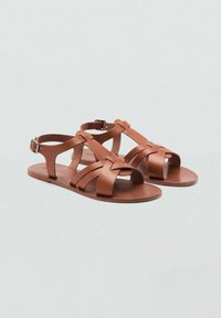 Sandali in pelle marrone con cinturini incrociati, fibbia regolabile alla caviglia e suola piatta. Progettati per traspirabilità e comfort.