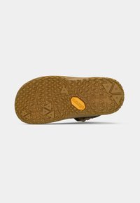 Semelle de chaussure marron avec un motif de semelle en forme de triangle et un logo Vibram orange au centre sur un fond blanc.