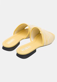 Pair of yellow slip-on sandals with low black heels and white striped fabric across the toes on a plain light background.