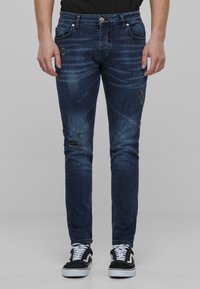 Uskeđe skinny tamnoplave traperice s pojačanim detaljima, suptilnim izbljeđivanjem, pet džepova i petljicama za remen, uparen s crno-bijelim tenisicama.