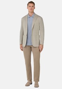 Svetlo siva blazer s zarezanimi reverji, svetlo modra polo majica, bež chinos hlače in bež loafer čevlji. Teksturna tkanina in sproščen kroj.