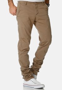 Khaki cotton chinos with a slim fit, featuring side pockets and button closure, paired with white sneakers. Smooth texture and minimalistic design.