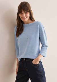 Ljusblå ribbad topp med båthalsringning och trekvartsärmar, ihop med mörka jeans i klassisk skärning med synliga sömmar.