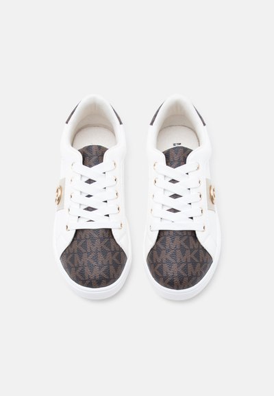 Par belih superg z rjavimi vzorčastimi kapicami in jezički na prstih, z zlatimi poudarki in belimi vezalkami, pogled z vrha na belem ozadju.