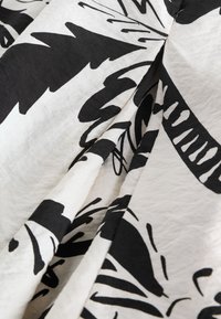 Tissu blanc avec des motifs abstraits de feuilles et de lignes noires audacieux, présenté avec des plis doux et des détails de texture.