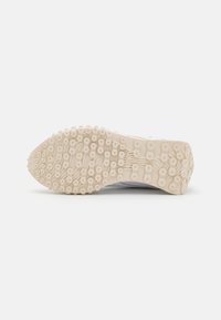 Semelle de chaussure de sport en matériau en caoutchouc beige avec des motifs de traction circulaires, conçue pour l'adhérence et la stabilité. Surface légèrement texturée.