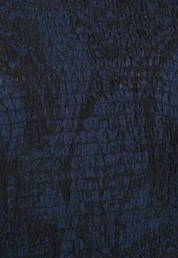Texturierter Stoff in Dunkelblau und Schwarz, mit einem zerknitterten Muster und unregelmäßigen, wellenartigen Linien. Weiche Oberfläche mit unterschiedlichen Tiefen.