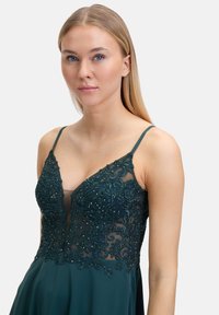 Zielona sukienka w kolorze szmaragdowym z dopasowanym gorsetem, ozdobiona skomplikowanymi koralikami i haftem kwiatowym, oraz zwiewną spódnicą. Regulowane cienkie ramiączka.