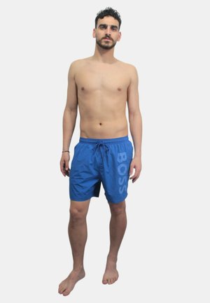 Pantalones de baño azules con cintura ajustable, que presentan un gran logo blanco "BOSS" en el lado izquierdo, fabricados en un material ligero y de secado rápido.