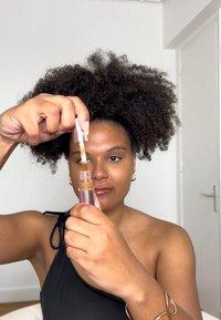 Applicateur de fond de teint avec une bouteille en plastique transparente et un capuchon métallique. Le liquide est d'une teinte brune. Le sujet le tient d'une main, montrant les détails.