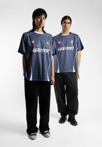 Jūras zilas futbola krekls ar baltām akcentiem un režģa rakstu, ar "Wasted" logotipu. Apvienots ar melniem vaļējiem biksēm un sporta apaviem.