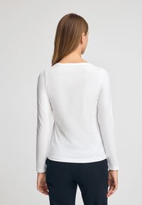 Biała koszula z długim rękawem i okrągłym dekoltem, o gładkiej, miękkiej fakturze. Tył jest prosty, bez dodatkowych elementów.