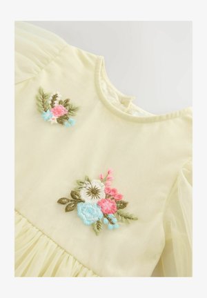 Šviesiai geltona suknelė, dekoruota rožių, mėlynų ir baltų gėlių siuvinėjimu. Pūkinės rankovės, klostuota sijonas ir apvalus iškirpimas su sagtimi nugaros pusėje.