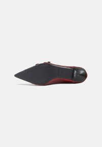 Zapato de punta afilada con un upper rojo brillante, suela negra delgada, textura suave y diseño minimalista. Tamaño indicado como 37.