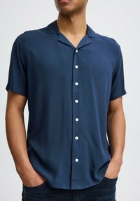 Camicia a maniche corte con bottoni in tessuto blu scuro, dotata di colletto alla camicia, otto bottoni bianchi e una vestibilità comoda con una texture liscia.