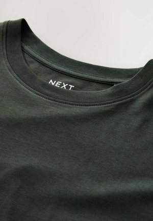 Tamnozelena pamučna majica kratkih rukava s okruglim izrezom i rebrastim ovratnikom. Ima bijeli „NEXT” logo na unutarnjoj oznaci ovratnika. Glatka tekstura.