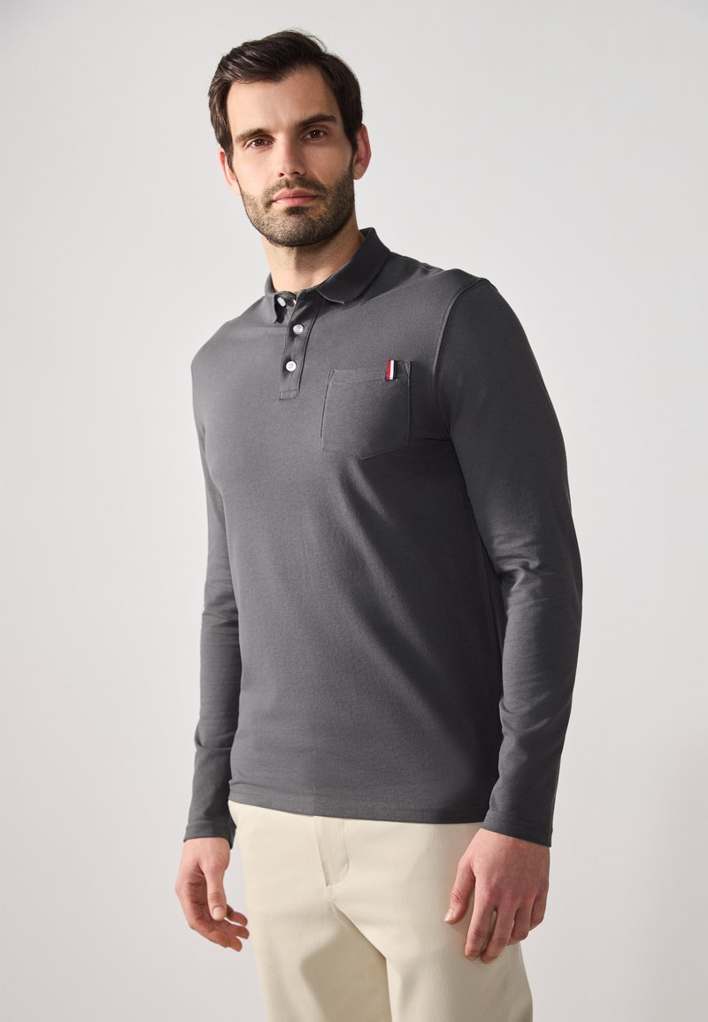 Grå langermet polo skjorte med krage, med en brystlomme, 3-knaps placket, og en liten rød, hvit og blå detalj.