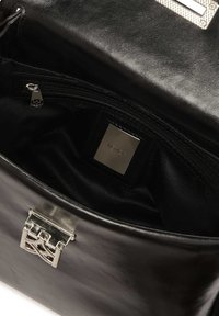 Čierna kožená kabelka s hladkým povrchom, vybavená strieborných kovaniami a vnútornou vreckom na zips. Logo štítok viditeľný vo vnútri.