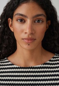 Capo a maglia con un motivo a disegni in bianco e nero. Presenta una scollatura rotonda, tessuto testurizzato e qualche dettaglio di pelle visibile.