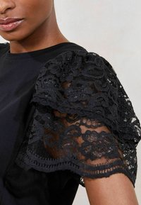 Black top featuring short sleeves made of intricate black lace with floral patterns and embellishments, combined with a smooth cotton body.