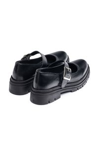 Zapatos Mary Jane de piel negra con puntera redondeada, suela plana y correa ajustable con hebilla plateada. Acabado texturizado.