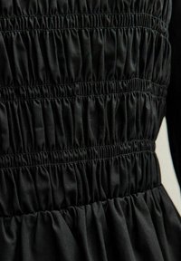 Czarna sukienka z marszczonym materiałem z elastycznym ściąganiem, gładką fakturą i rozszerzanym dołem. Brak widocznych wyraźnych wzorów lub elementów metalowych.