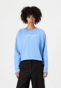 Felpa blu chiaro con maniche raglan, caratterizzata da un logo bianco in corsivo "Hugs" sul davanti, realizzata in morbido tessuto di cotone.