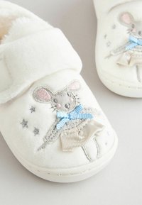 Chaussons en peluche blancs avec une texture douce, présentant un design de souris brodé en gris, bleu et crème, avec des accents décoratifs.