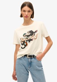 T-shirt in cotone crema con una grafica vivace di un pantera e un serpente, con testo decorativo in beige e accenti colorati. Vestibilità casual.