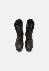 Botas de cuero negro con cordones, que presentan un caño alto, textura suave y detalles decorativos en el cuello interno. Suela de goma para mayor tracción.
