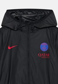 Zwarte windbreaker jas met een capuchon, rits aan de voorkant en logo's in rood en blauw: Nike aan de linkerzijde en Paris Saint-Germain met Qatar Airways eronder.