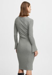 Abito a maniche lunghe a costine di colore grigio chiaro, con una silhouette aderente e maniche a campana, che arriva fino a metà polpaccio. Tessuto morbido.