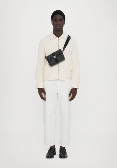 Veste zippée blanche, sac bandoulière noir avec des accents métalliques, pantalon blanc et mocassins noirs. Design simple avec un look élégant et moderne.