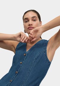 Sukienka dżinsowa z głębokim dekoltem w kształcie litery V, krótkimi rękawami i drewnianymi guzikami. Tkanina ma gładką fakturę i średni niebieski kolor.