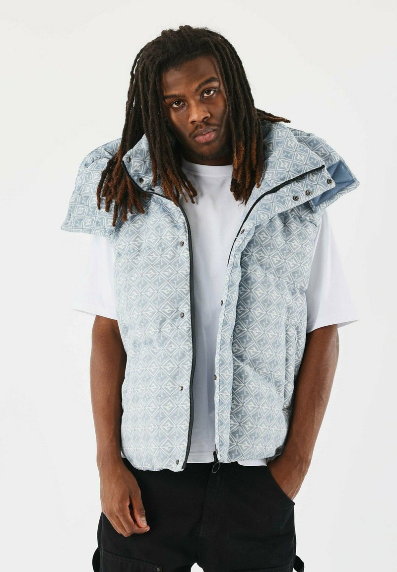 Lichtblauw met patroon vest met een hoge kraag, drukknoopsluitingen en een relaxte pasvorm, gedragen over een wit T-shirt en gecombineerd met donkere broek.