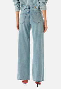 Jeans de tiro alto y pierna ancha en azul claro con una textura de denim clásica, cinco bolsillos y dobladillos deshilachados, combinados con tacones rojos.