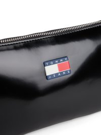 Čierna lesklá klopnová taška so zipsovým uzáverom, ktorá má modrý a červený obdĺžnikový nášivku s nápisom "TOMMY JEANS." Hladká textúra.