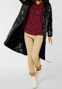 Abrigo inflable negro con textura brillante, camisa de leopardo rosa, pantalones beige y zapatillas blancas. El abrigo tiene cierre con cremallera y capucha.