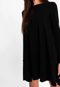 Abito nero a maniche lunghe realizzato in tessuto morbido e fluido; presenta un colletto rotondo e una silhouette a A. Nessun motivo distintivo o accessorio.