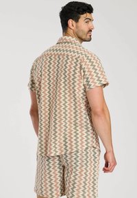 Conjunto de camisa de manga corta y pantalones cortos en un patrón de zigzag de color beige, rosa suave y verde. Tela texturizada, con detalle de cuello y bolsillo en el pecho.