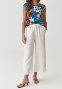 Top floreale con maniche a cappuccio, in blu, verde e rosa; abbinato a pantaloni in lino bianchi con vita elasticizzata e gamba dritta.