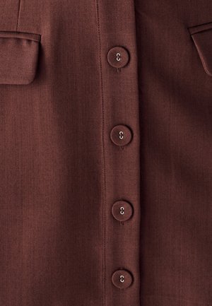Bordo srajca iz gladkega, teksturiranega blaga z gumbom spredaj. Dva žepa na prsih in šest okroglih gumbov z rahlim leskom.