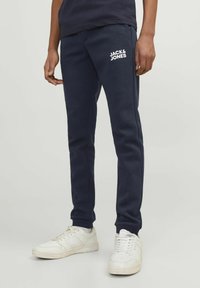 Marineblauwe katoenen sweatpants met elastische boorden, voorzien van een witte logo-opdruk op de linker bovenbeen. Gepaard met witte sneakers.