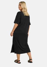 Svart oversized t-shirt klänning med korta ärmar och sidofragor, tillverkad av mjukt tyg. Har en avslappnad passform och når nedanför knäna.