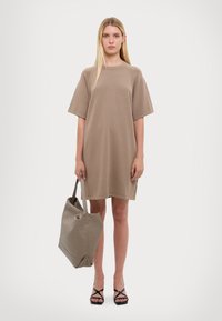 Khaki oversized tričko šaty s krátkym rukávom, mäkká tkanina, zaoblený výstrih, v kombinácii s béžovou taškou a čiernymi sandálmi na viazanie.