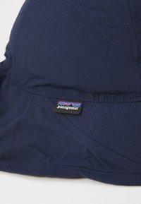 Un chapeau seau bleu marine en tissu lisse ; il comporte des détails cousus et un petit logo noir Patagonia sur le côté.