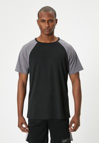 Sort og grå atletisk t-shirt med korte ærmer, rund halsudskæring og en glat tekstur; har kontrasterende raglan-ærmer.