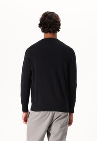 Maglione da uomo blu navy, con collo rotondo, maniche lunghe, polsini e orlo a costine, realizzato in un morbido materiale lavorato a maglia, abbinato a pantaloni grigi chiari.