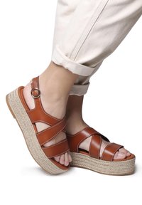 Sandali platform in pelle marrone con cinturini incrociati, un anello alla caviglia rotondo e suola in stile juta intrecciata, caratterizzati da una finitura liscia e cuciture leggere.