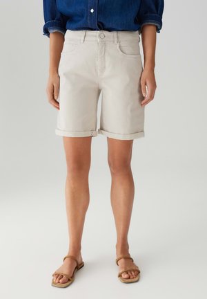 Shorts in denim beige con chiusura a singolo bottone, risvolti, e tasche frontali, abbinati a sandali piatti marroni.